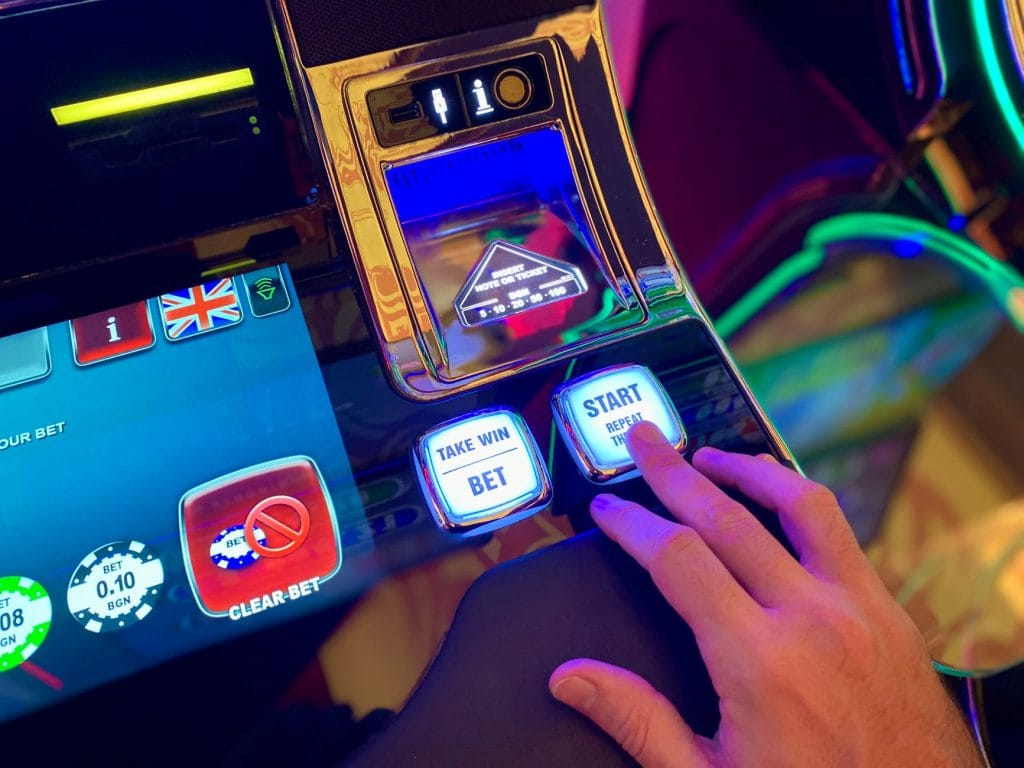 MP 1.394 proíbe bets no Brasil e define prazo para saque de saldos Mão interage com botões de uma interface digital colorida de máquina caça-níqueis.