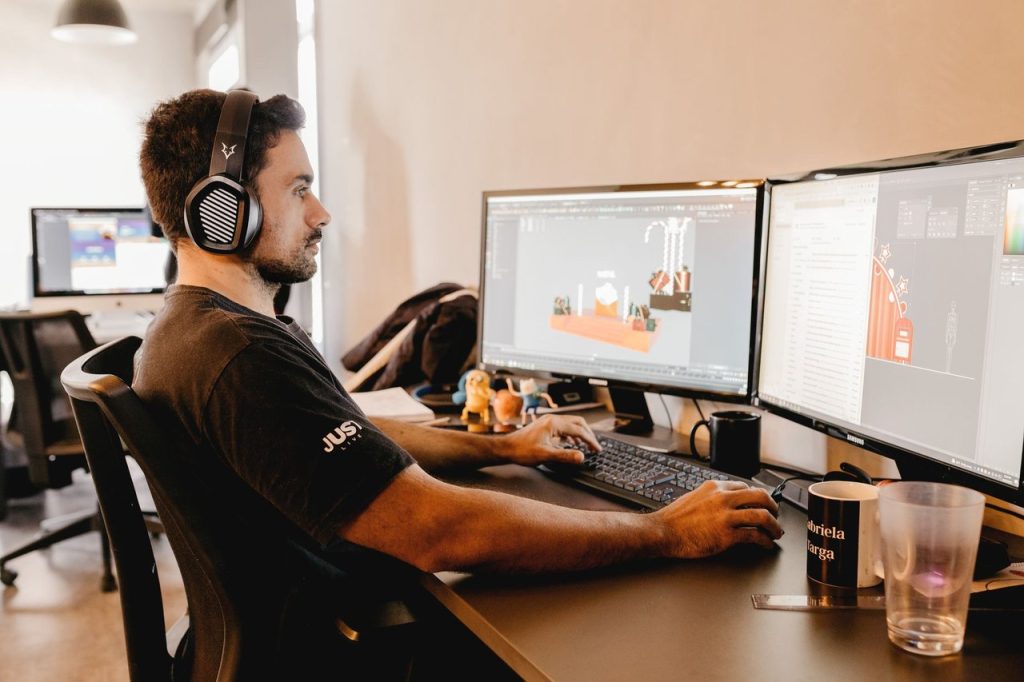 Regulamentação do Marco Legal dos Games cria programa de apoio ao setor no Brasil Profissional usando fones de ouvido trabalha diante de dois monitores em um ambiente moderno de tecnologia.